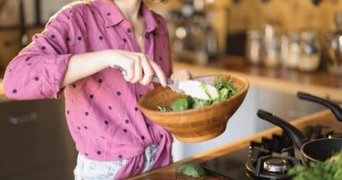 Kadın salatayı roka ve pancar yapraklarıyla karıştırıyor. Tahta kasede. Evde sağlıklı vejetaryen yemekleri pişirmek.