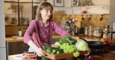 Genç bir kadın evdeki mutfak tepsisine taze sebze ve sebze dolu tahta tepsi koyuyor. Sağlıklı yaşam tarzı ve sağlık konsepti. Vejetaryenlik fikri