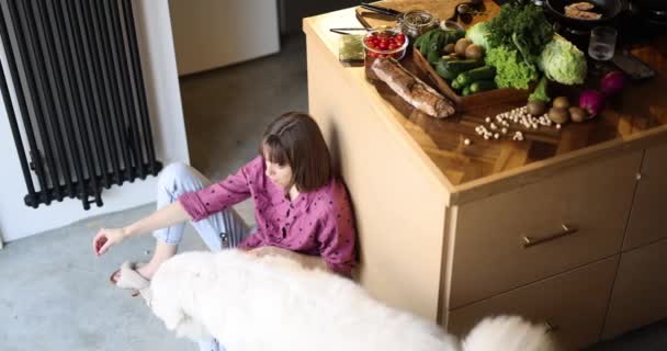 Young Woman Eating Salad Feeding Her Huge Adorable White Dog — Video