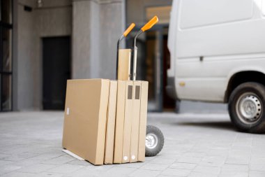 Folding furniture in cardboard boxes on a pushcart delivered by vehicle near building entrance. Concept of home delivery