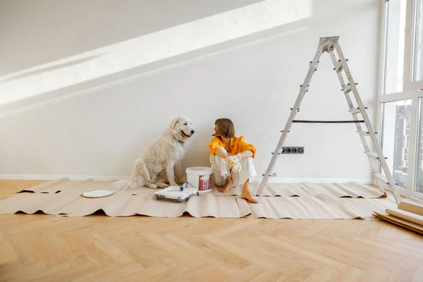 Young woman sits with her dog in room while making repairing in apartment. Repair and house renovation concept, friendship with pet