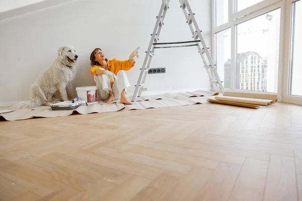Young woman sits with her dog in room while making repairing in apartment. Repair and house renovation concept, friendship with pet