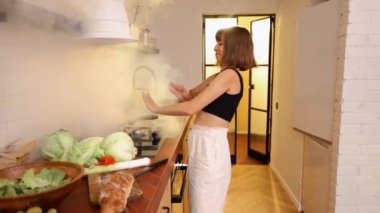 Mutfakta yanan yemeklerden çıkan duman yüzünden panikle el sallayan bir kadın. Genç ev hanımı mutfakta bir köpekle yemek pişiriyor.