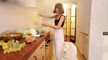 Mutfakta yanan yemeklerden çıkan duman yüzünden panikle el sallayan bir kadın. Genç ev hanımı mutfakta bir köpekle yemek pişiriyor.