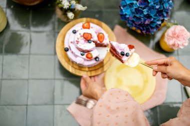 Female cuts berry cheese cake on table decorated with flowers, view from above, Sweet holiday concept