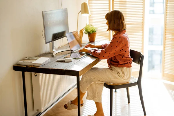 自宅の日当たりの良い部屋で木製のテーブルに座っている間 女性はコンピュータ上で動作します 居心地の良い雰囲気で自宅からのリモートワークの概念 — ストック写真