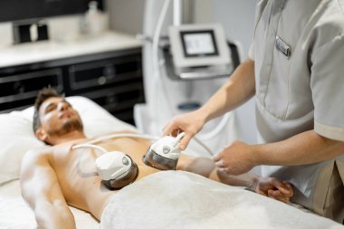 Man receiving vacuum roller massage on belly arrea at medical beauty centre. Lymphatic drainage massage procedure