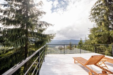 Doğada ahşap şezlonglu geniş bir teras. Çam ağaçları ve dağlar manzaralı.