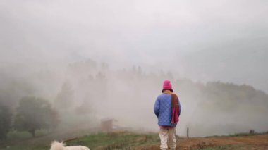 Sisli dağların güzel manzarası ve parlak elbiseli insan sabah vakti çayırda bir köpekle yürüyor.