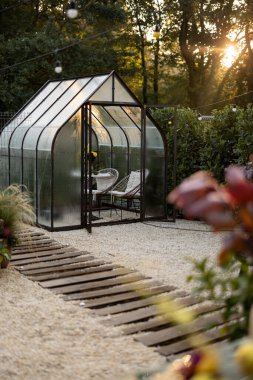 Arka bahçede sabah manzarası paslı metalden yapılmış güzel bir sera ve içinde masa ve çiçekler olan cam.