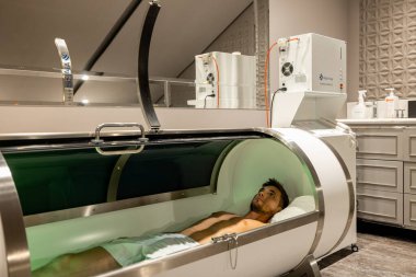 Man lying in oxygen capsule, having deep rest and recovery during the medical procedure of filling the body with oxygen