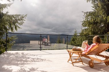 Dağlardaki geniş beyaz bir terasta dinlenirken, bir kadın dinlenme odasında uzanıyor. Eğlence ve doğa kavramına kaçmak