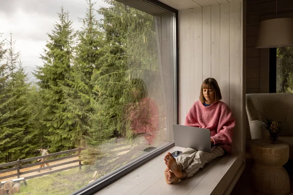 Kadın Dağların Manzarası Harika Olan Bir Pencerede Otururken Dizüstü Bilgisayarla — Stok fotoğraf