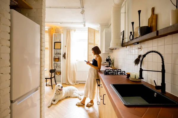 Mulher Usa Telefone Inteligente Enquanto Está Com Seu Cão Cozinha — Fotografia de Stock