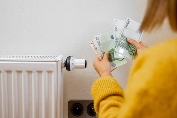 Person holding euro banknotes near heater at home. Concept of expensive energy resources and the energy crisis in Europe