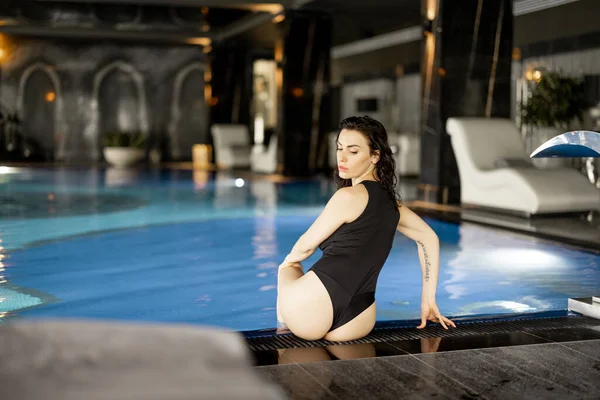 Woman Black Swimsuit Sitting Relaxed Swimming Pool Indoors Spending Holidays — Stok fotoğraf