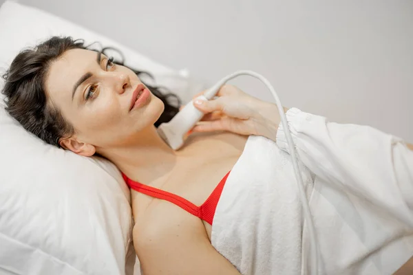 Beautiful adult woman during an ultrasound examination of thyroid gland, lying at medical office. Endocrine system health concept