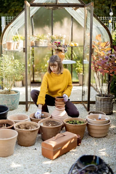 Жінка Вирощує Квіти Глиняних Глечиках Сидячи Перед Красивою Скляною Оранжереєю — стокове фото