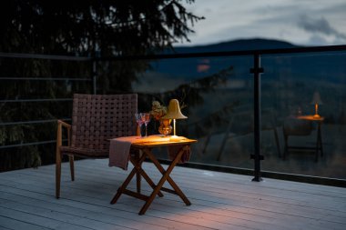 Gün batımında dağlarda rahat bir masa, sandalye ve lamba bulunan geniş bir teras. Evde dinlenmek için rahat bir dinlenme yeri.
