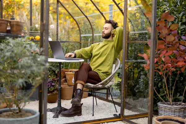 Ember Laptopon Dolgozik Miközben Kerek Asztalnál Üvegházban Növényekkel Virágokkal Udvaron — Stock Fotó