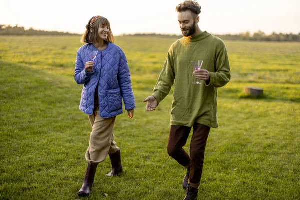 日落时分 穿着华丽衣服的男人和女人一边在绿茵的草坪上一起散步 一边热情地交谈着 情侣们在大自然上度过秋天的闲暇时光 — 图库照片