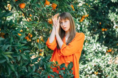 Turuncu elbiseli kız portakal bahçesinde el ele tutuşarak kameraya poz veriyor. 