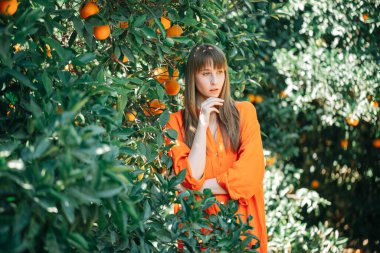 Turuncu elbiseli kız portakal bahçesinde el ele tutuşarak düşünüyor. 