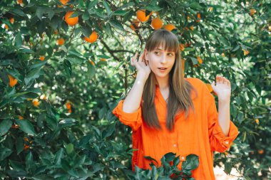 Turuncu elbiseli genç kız, portakal bahçesinde el ele tutuşarak başını çeviriyor. 