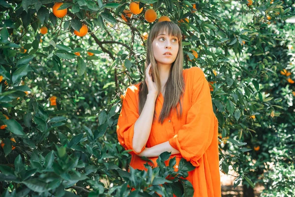 Young girl in orange dress is thinking by looking up in orange garden 