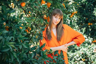 Turuncu elbiseli genç kız, portakal bahçesindeki Ron Belini bir arada tutarak kameraya bakıyor. 