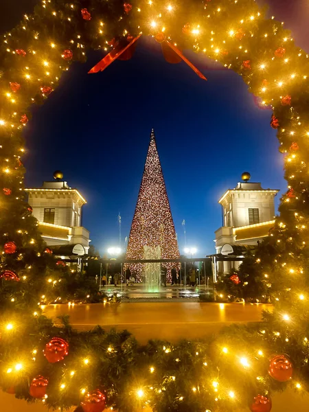 Gün batımında mavi gökyüzünün arka planındaki ışıklandırılmış Noel ağacı ve Noel ışıkları ve fiyonklarıyla dekorasyon çerçevesi.