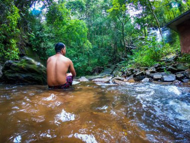 Yeşil ormanlardaki doğal şelalede farklı açılardan sessiz bir adam.