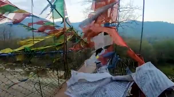 鉄の吊橋に立っている若い男は午前中に沈黙の中で多くの仏教の旗を掲げて — ストック動画