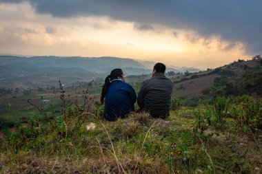 Genç çift dağın tepesinde oturuyor sisli tepe arkaplanı ve dramatik gökyüzü ile sabah görüntüsü Badda Peak Shillong Meghalaya Hindistan 'da çekiliyor..