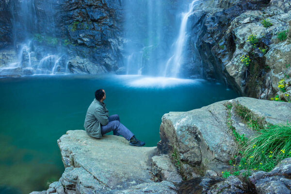 young man watching waterfall falling from mountain with calm blurred water surface at morning image is taken at thangsning fall shillong meghalaya india.