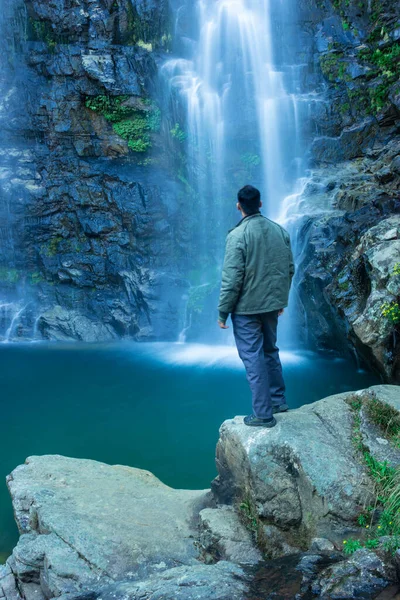 Şelalenin dağdan düşüşünü izleyen genç adam sabah bulanık su yüzeyi ile Şükran Günü görüntüsü Shillong Meghalaya Hindistan 'da çekilmiştir..