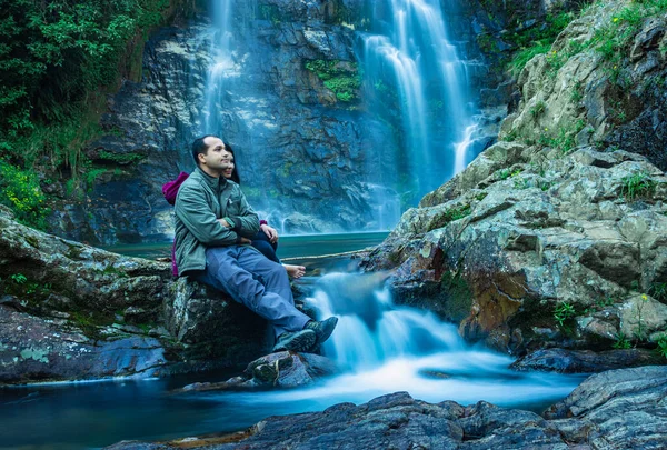 Şelaleyle dağdan düşen ve sabah bulanık su yüzeyi olan kayalıklarda oturan çift, Şillong Meghalaya Hindistan 'da çekiliyor..