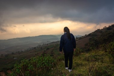 Sisli tepe arkaplanı ve sabah dramatik gökyüzü ile dağın tepesinde duran genç kız Badda Peak Shillong Meghalaya Hindistan 'da çekilmiştir..