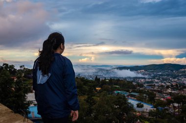 Şehir merkezindeki şehir manzarasını seyreden genç bir kız, akşam üzeri dağdan dramatik bulutlu bir gökyüzü ile Hindistan 'ın Shillong meghalaya bölgesinde çekiliyor..