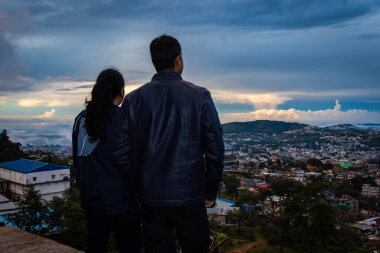 Şehir merkezindeki şehir manzarasını seyreden genç bir çift, akşam üzeri dağların tepesinden dramatik bulutlu gökyüzü görüntüsüyle, Şillong meghalaya Hindistan 'da çekiliyor..