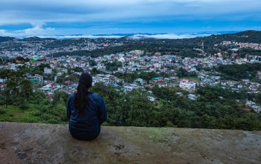 Şehir merkezindeki şehir manzarasını seyreden genç bir kız, akşam üzeri dağdan dramatik bulutlu bir gökyüzü ile Hindistan 'ın Shillong meghalaya bölgesinde çekiliyor..