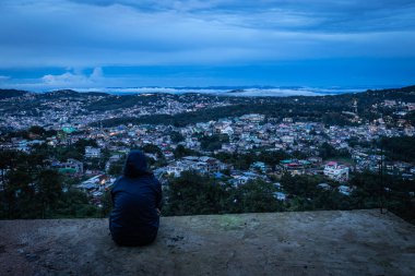 Şehir merkezindeki şehir manzarasını seyreden genç bir kız, akşam üzeri dağdan dramatik bulutlu bir gökyüzü ile Hindistan 'ın Shillong meghalaya bölgesinde çekiliyor..