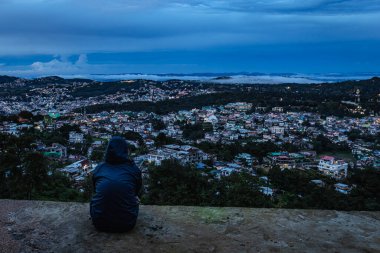 Şehir merkezindeki şehir manzarasını seyreden genç bir kız, akşam üzeri dağdan dramatik bulutlu bir gökyüzü ile Hindistan 'ın Shillong meghalaya bölgesinde çekiliyor..