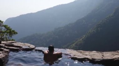 Adam dağ yamacındaki doğal yüzme havuzunun en üst açılarından el değmemiş manzarasının keyfini çıkarıyor.