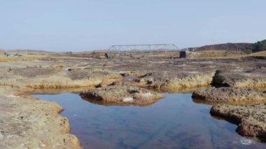 Kuru nehir kayalıkları ve arkaplanda demir köprü var.