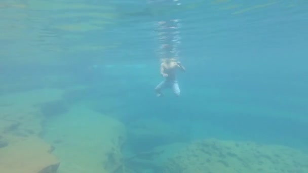 年轻人穿着蓝色水晶般清澈的衣服在瀑布的水面上从高处游着 — 图库视频影像