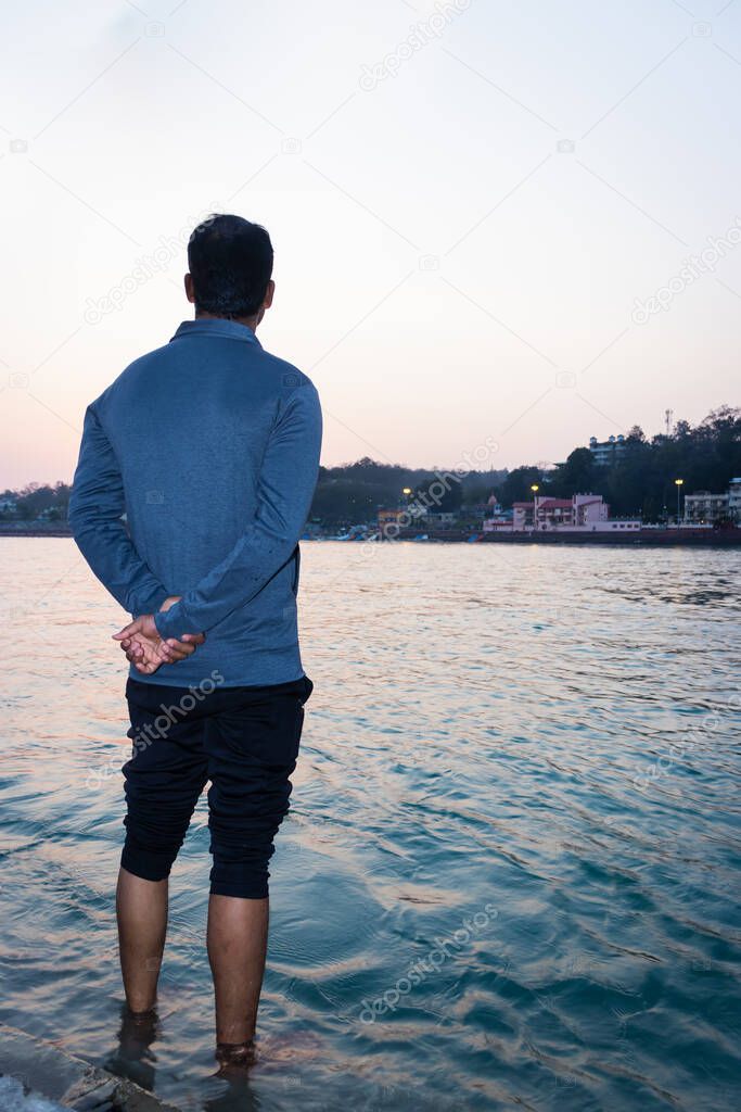 isolated young man standing at ganges river bank from flat angle image is taken at ganga river bank rishikesh uttrakhand india.