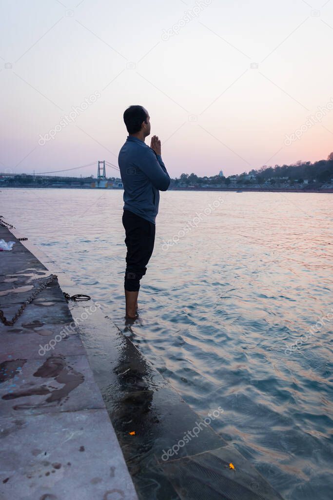 isolated young man prying the holy ganges river at river bank from flat angle image is taken at ganga river bank rishikesh uttrakhand india.