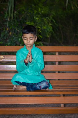 Genç bir çocuk, geleneksel elbisesiyle ahşap bankta farklı açılardan meditasyon yapıyor.