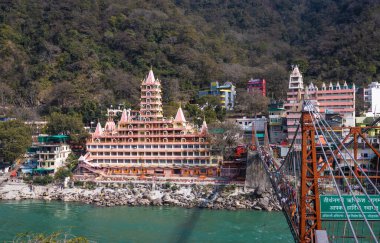 Gangsterler nehir kıyısındaki eski Hindu tapınağı. 15 Mar 2022 'de Hindistan' daki Lakshman jhula rishikesh uttrakhand tapınağında gün içinde düz açılı görüntüden demir köprü başı çizgisi çekiliyor..